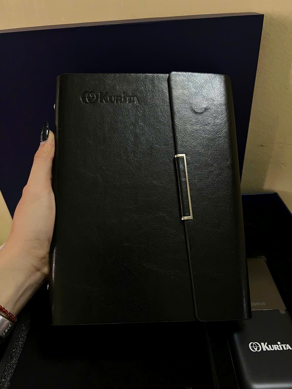 Black leather ring-bound notebook with the Kurita logo debossed on the cover and a metal clasp