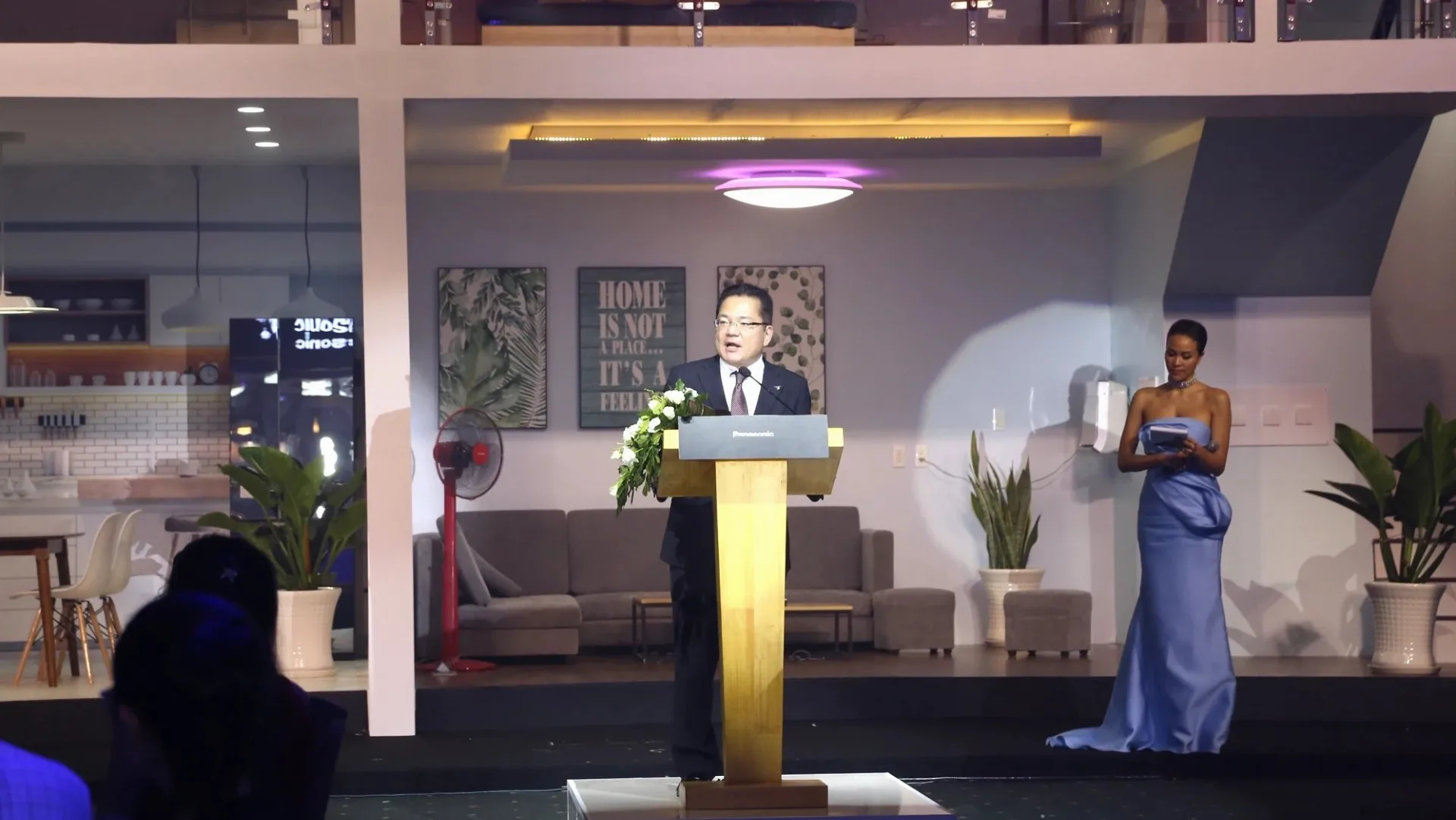 Panasonic representative speaking on a stage built as a home with lighting, fans and electrical devices