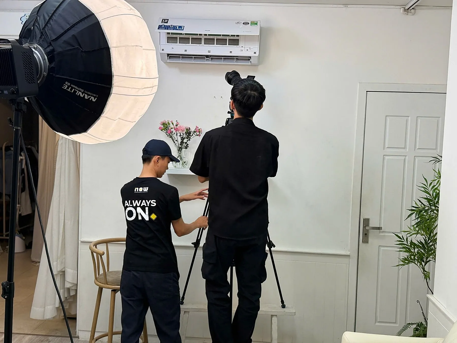 Now Agency crew adjusting a camera beneath an AUX air conditioner on the sitcom set